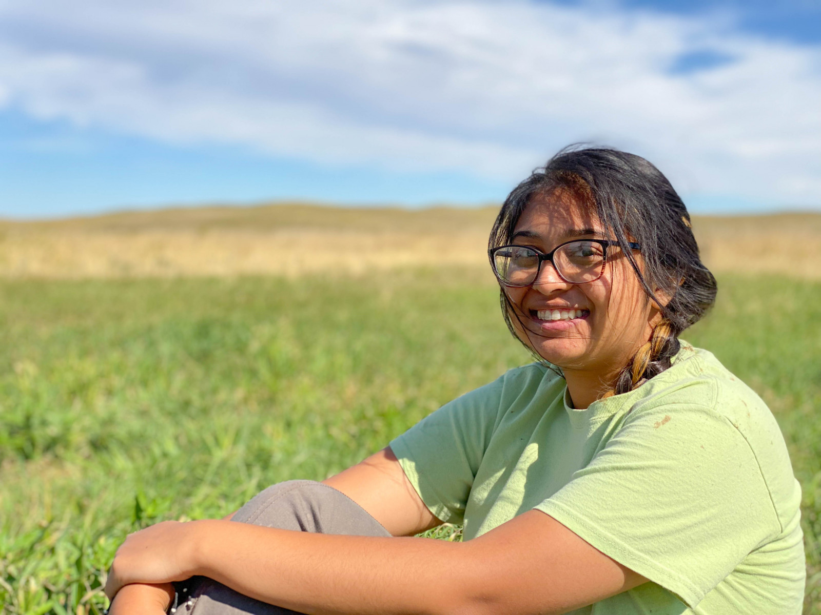 Vidya sits in a green field and smiles at the camera.